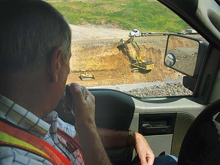 Project Manager Jim Smith radios to crew members below as he monitors job progress from an access road higher up the mountain. With the projects steep angles, narrow work area, hard rock and many environmental protocols, Smith calls it the toughest job Ive ever worked on in my 42 years in this business.  (Photo by Carl Thiemann)